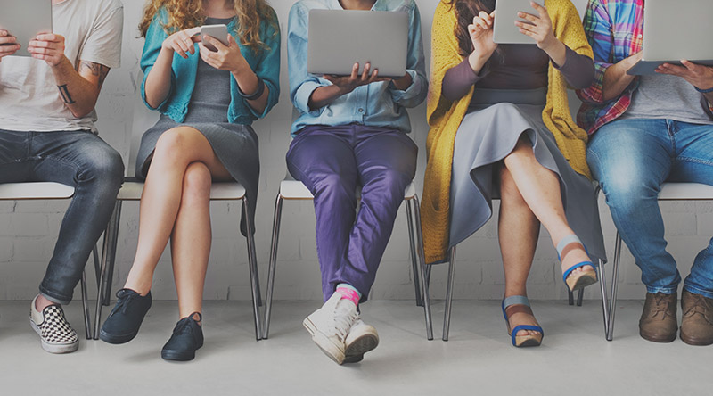 five people sat on chairs looking at different hand held devices
